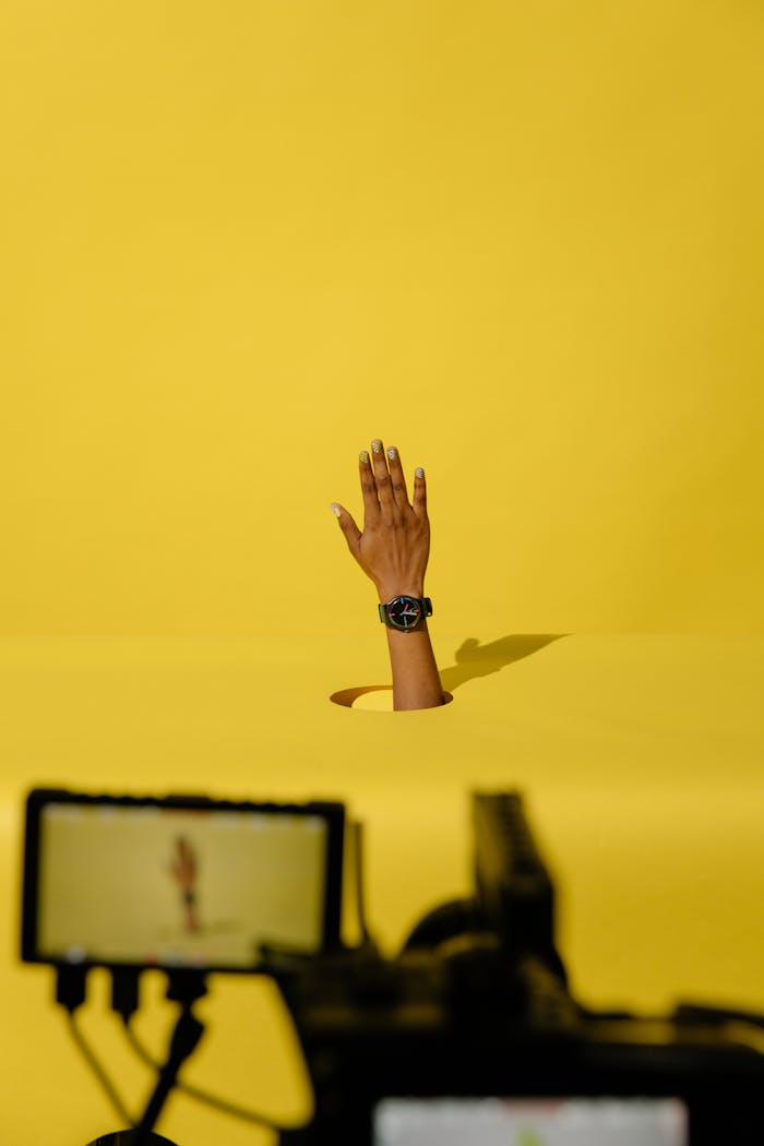 A unique hand gesture breaking through yellow backdrop in a studio setting.