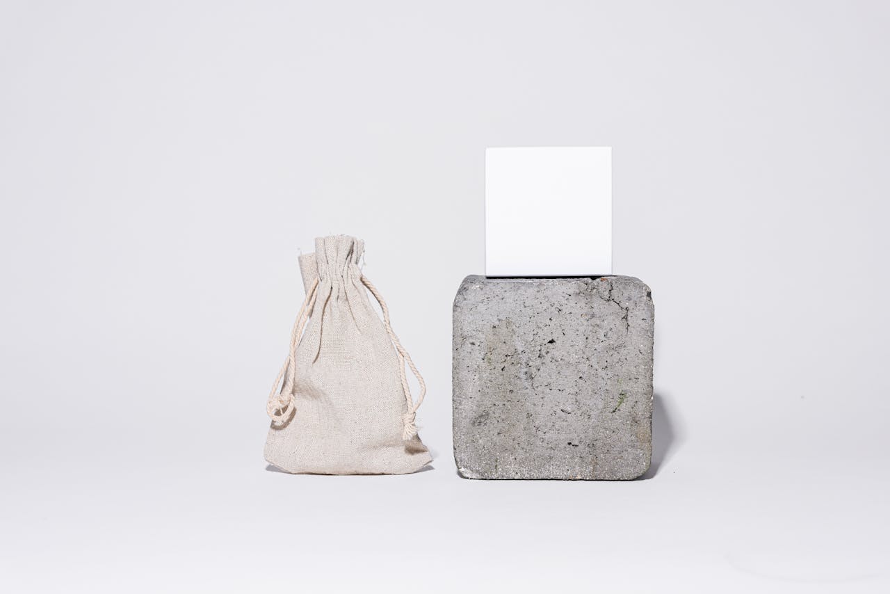 A minimalist studio shot featuring a fabric bag and a stone cube against a white background.